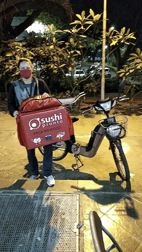 Entregador ao lado da bicicleta segurando a bag adesivada da Sushi Pronto